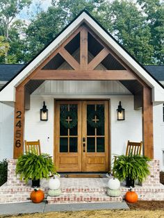 two wooden chairs sitting on the front porch of a white house with pumpkins and greenery