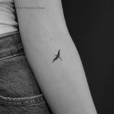 a black and white photo of a small bird tattoo on the left inner arm by little tattoos