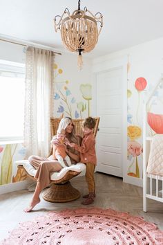 a woman sitting in a wicker chair with a baby on her lap and a chandelier hanging from the ceiling