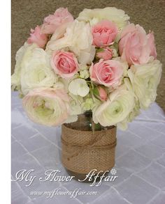 a vase filled with pink and white flowers on top of a cloth covered tablecloth