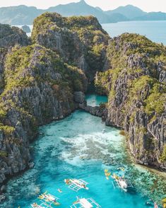 several boats floating in the water near some cliffs and mountains with blue water surrounded by green vegetation