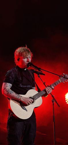 a man holding a guitar while standing in front of a microphone on top of a stage