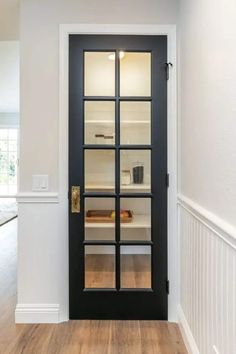 an empty room with a black door and white trim on the walls, along with hardwood floors