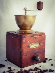 an old fashioned coffee grinder sitting on top of a wooden box filled with coffee beans