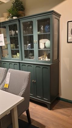 a green china cabinet with glass doors on the front and side, next to a white dining room chair