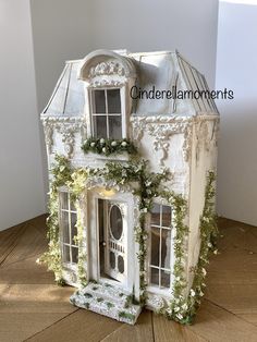 a white doll house with ivy growing on the roof and windows, sitting on top of a wooden floor