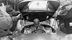 a group of men standing around a car looking at the driver's headlight