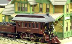 a toy train is on the tracks in front of a model house and other buildings