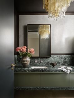 a bathroom with marble counter tops and gold chandelier above the sink, along with pink flowers