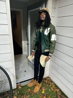 a man with long hair wearing a green jacket and hat standing in front of a door