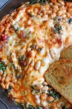 a skillet filled with baked beans and spinach next to two slices of bread