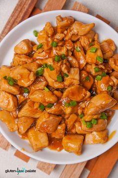 a white plate topped with chicken covered in sauce and garnished with green onions