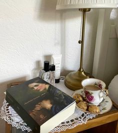 a table with a book, cup and saucer on it next to a lamp