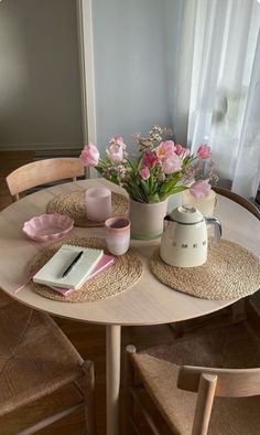 a table with flowers and books on it in front of a window next to two chairs