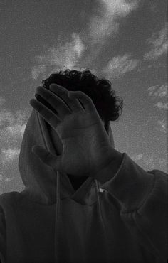 black and white photograph of a man covering his face with both hands while looking up at the sky