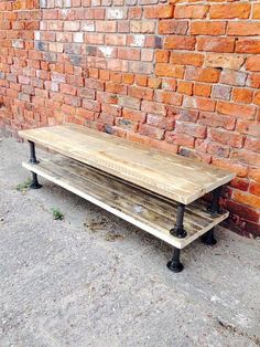 a wooden bench sitting in front of a brick wall with black pipe legs on it