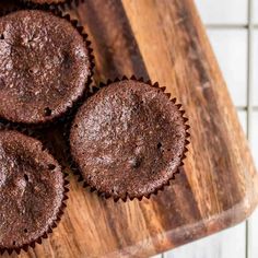 three chocolate cupcakes sitting on top of a wooden cutting board