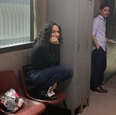 a woman sitting on top of a chair next to a man in a locker room