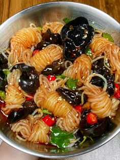 a bowl filled with pasta and olives on top of a wooden table next to a person's hand