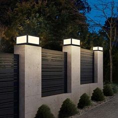 three lights that are on the side of a wall next to some bushes and trees