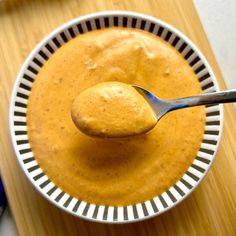 a spoon in a bowl filled with yellow sauce on top of a wooden cutting board