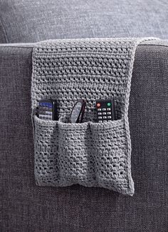 a crocheted pocket holds four remotes on the arm of a gray couch