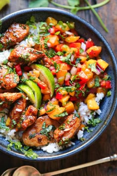 a blue bowl filled with rice, chicken and veggies next to cilantro