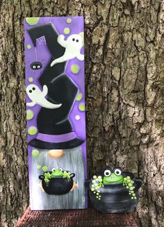 two halloween decorations are sitting on a shelf next to a tree with purple and black background