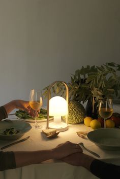 two people sitting at a table with food and wine in front of them, holding hands