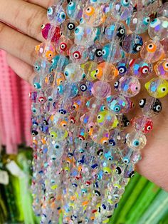 a hand holding a bunch of beads with eyes on them in front of a plant