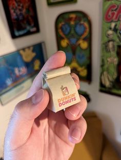 a person holding up a tiny donut in front of a wall with posters on it