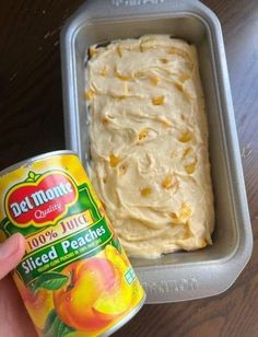 a hand holding a can of peach ice cream next to a container of sliced peaches