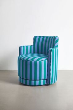 a blue and green striped chair sitting on top of a cement floor next to a white wall