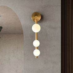 a wall light with three balls hanging from it's side next to a potted plant