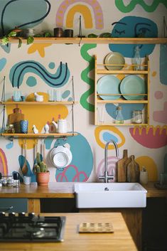 a kitchen with colorful wallpaper and open shelves above the sink, next to a stove