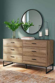 a wooden dresser sitting in front of a green wall with a round mirror above it