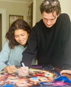 a young man and woman signing autographs for fans at a table in front of a poster