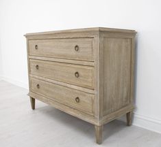 a wooden dresser sitting on top of a hard wood floor next to a white wall