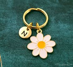 a gold key chain with a flower on it and a letter charm hanging from the end