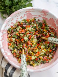 a bowl filled with chopped vegetables on top of a white and pink table cloth next to parsley