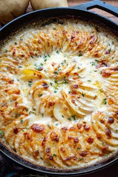 a baked dish with potatoes and cheese in a cast iron skillet on a wooden table