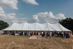 a group of people standing in front of a white tent on top of a grass covered field