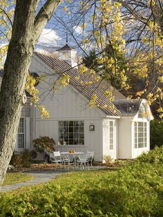 a white house sitting next to a tree with lots of yellow leaves on it's branches