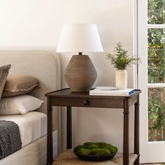 a small table with a lamp on top of it next to a bed and pillows