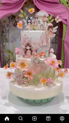 a three tiered cake decorated with pink flowers and fairy figurines on top