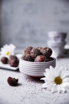 a white bowl filled with chocolate truffles next to two daisies on a table