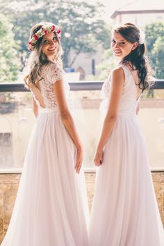 two beautiful young women standing next to each other wearing white dresses and flowers in their hair