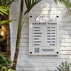 a sign on the side of a white brick building with palm trees in front of it