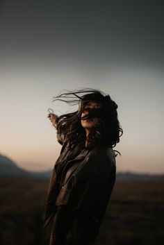 a woman with long hair standing in the middle of a field at sunset, looking into the distance