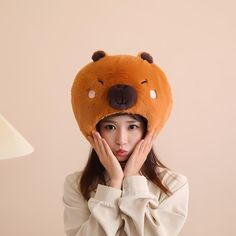 a woman wearing a brown bear hat with her hands on her face while standing in front of a lamp